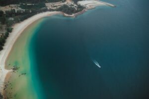 Aerial view of Kijal Beach, Terengganu with vibrant waters and a boat slicing through the sea.